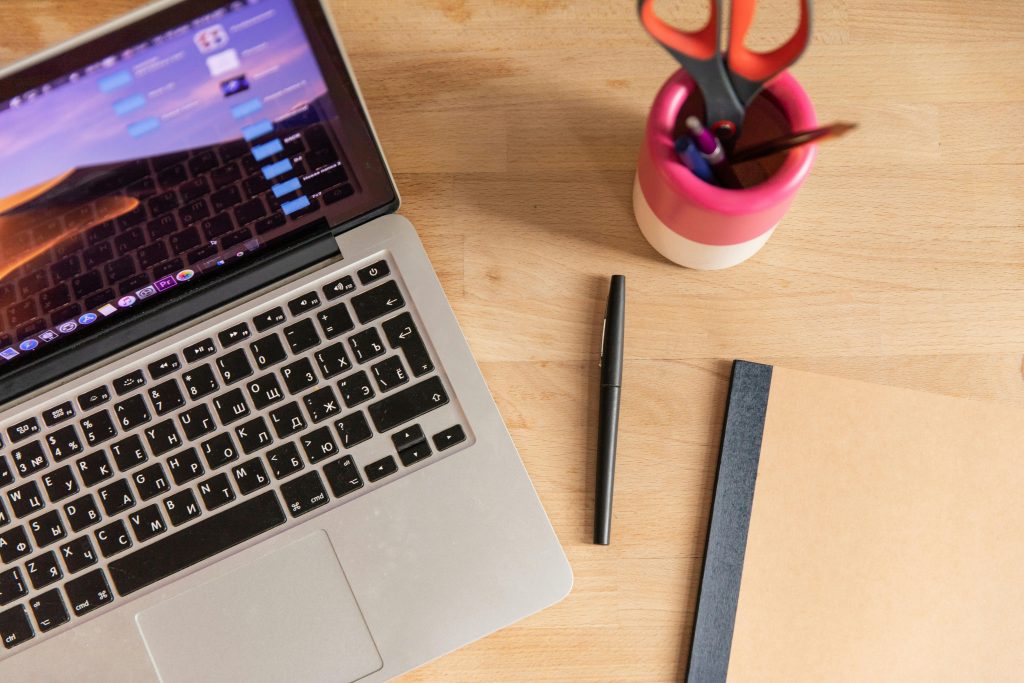 Pricing Top-down view of a laptop, pen, notebook, and scissors on a wooden desk, depicting a workspace setup.
